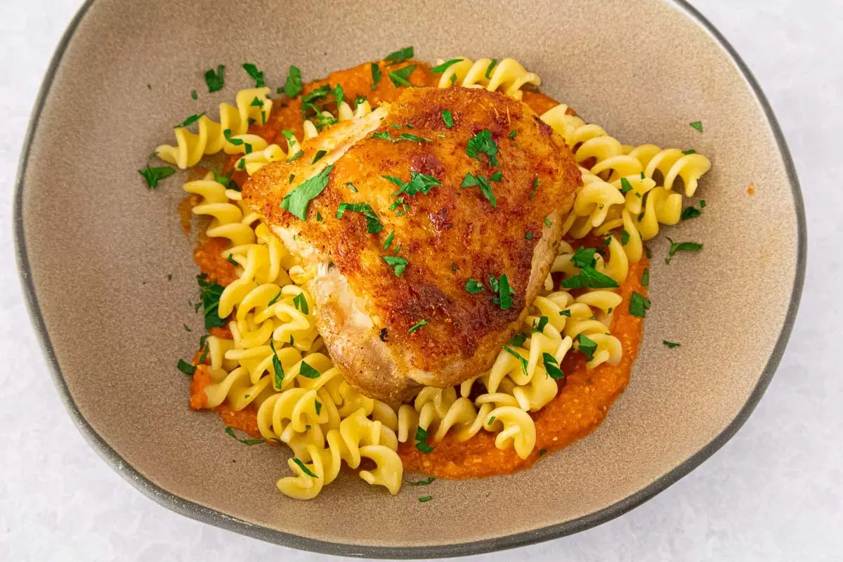 Crispy chicken romesco with fusilli pasta in a beige bowl.