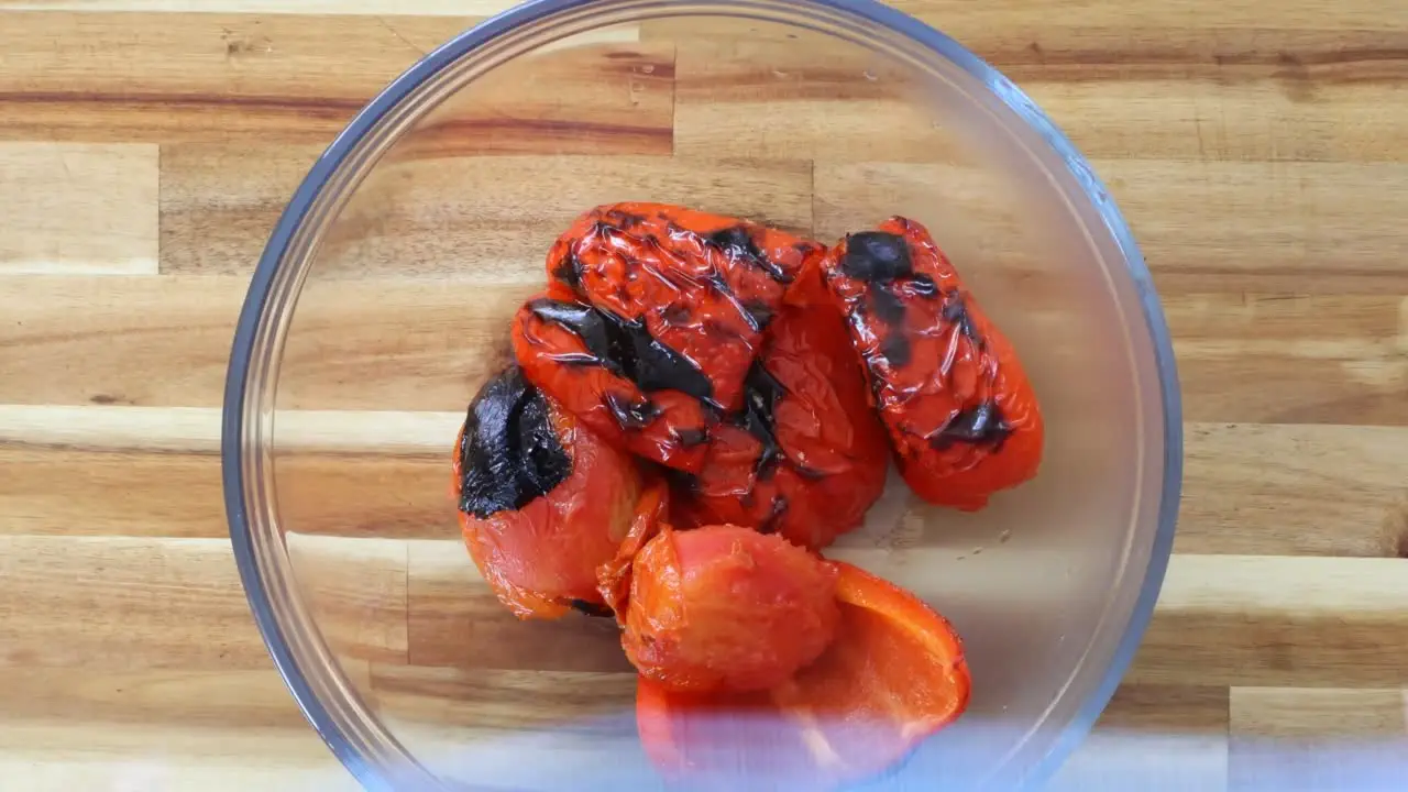 Roasted red bell peppers in a glass bowl on a wooden countertop.