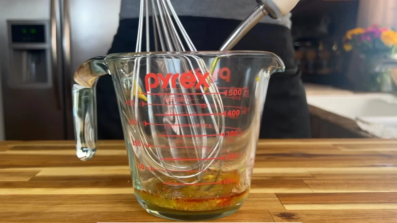 Person whisking ingredients in a Pyrex measuring cup on a wooden kitchen counter.