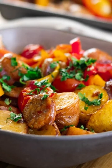 Delicious roasted sausage, peppers, and potatoes and herbs in a serving dish.