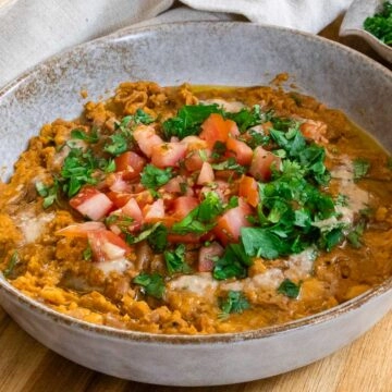 Mashed fava beans topped with fresh diced tomatoes and parsley in a rustic bowl.