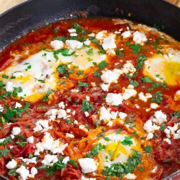 Savory Shakshuka in skillet with poached eggs, tomatoes, feta, and herbs. Perfect for a delicious breakfast or brunch.