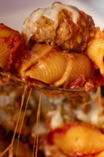 Cheesy pasta shells with meatball and tomato sauce in a spoon.