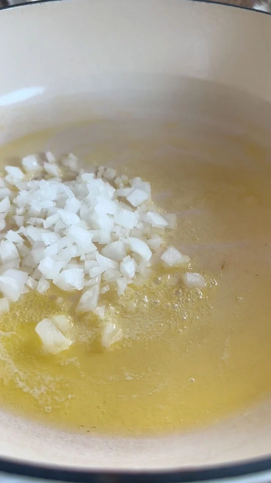 Chopped onions sautéing in melted butter in a white pan.