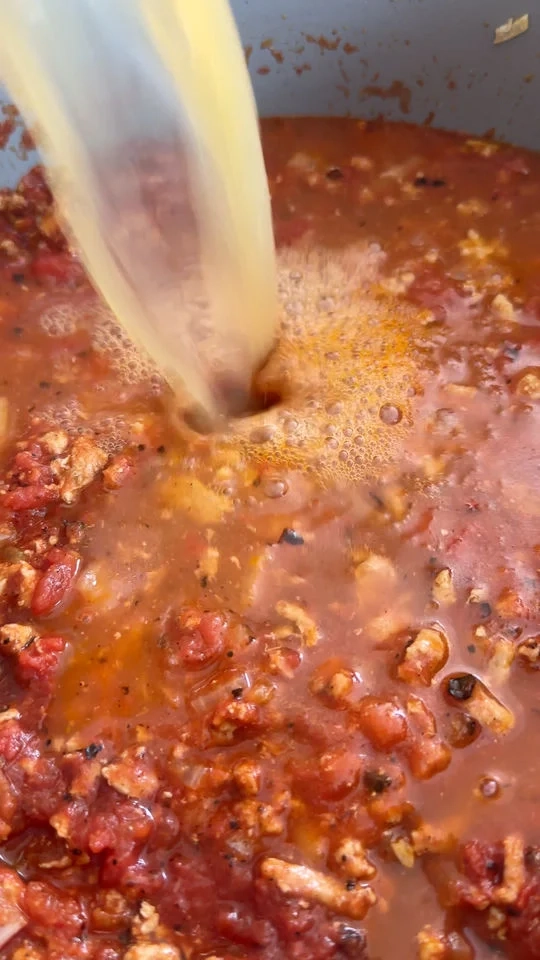 Pouring broth into a pot of tomato stew with ground meat.
