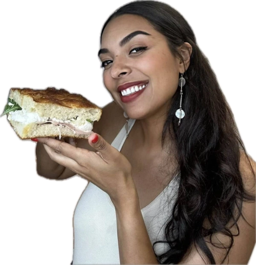 Smiling woman holding a large sandwich with layers of meat and lettuce.