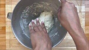 Hands kneading dough in a metal bowl on a wooden surface. Baking preparation at home.