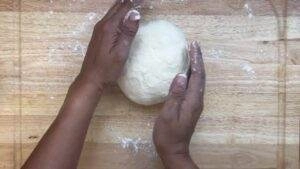Hands kneading round dough on a floured wooden board, preparing for baking.