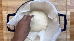 Hand preparing dough in a lined Dutch oven for bread baking.