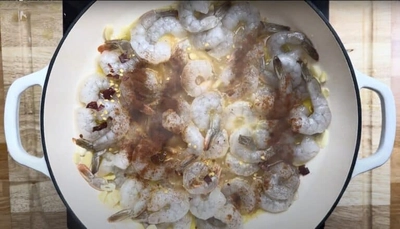 Shrimp cooking in a white pan with garlic and spices on a wooden surface.