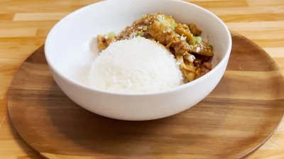 Bowl of rice and savory stir-fried dish with vegetables on a wooden plate, served on a wooden table.