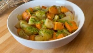 Bowl of roasted potatoes and sweet potatoes with green pesto sauce on a wooden table.