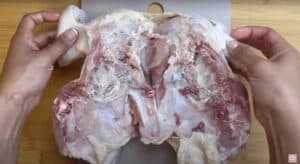 Raw chicken being prepared for spatchcocking on a cutting board.