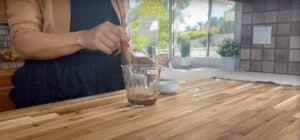 Person whisking sauce in a measuring cup in a bright kitchen setting.