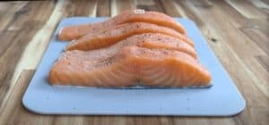 Fresh salmon fillets seasoned with pepper, ready for cooking on a blue cutting board.