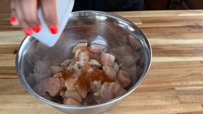 Seasoning raw chicken in a bowl with spices for a flavorful dish.