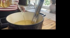 Pouring cooking oil into a pot with a candy thermometer in a kitchen setting.