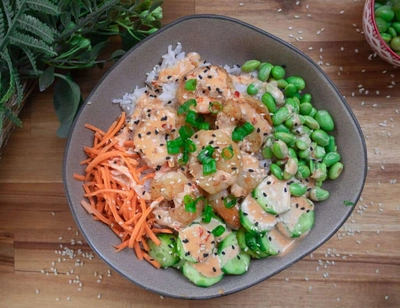 A delicious shrimp poke bowl with rice, edamame, cucumber, carrot, and sesame seeds, garnished with green onions.