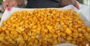 Tray of seasoned diced potatoes on parchment paper, ready for roasting.