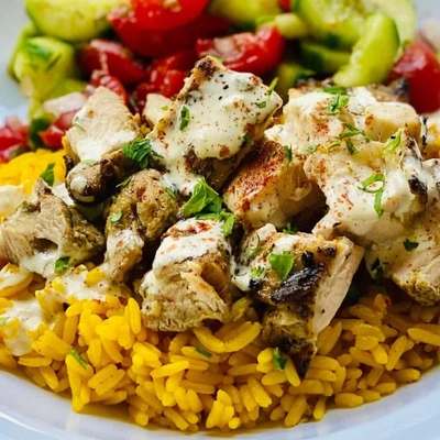 Chicken shawarma rice topped with creamy sauce, served with fresh cucumber and tomato salad.