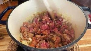 Cooking ground beef and onions in a Dutch oven; preparing a savory dish on a stovetop.
