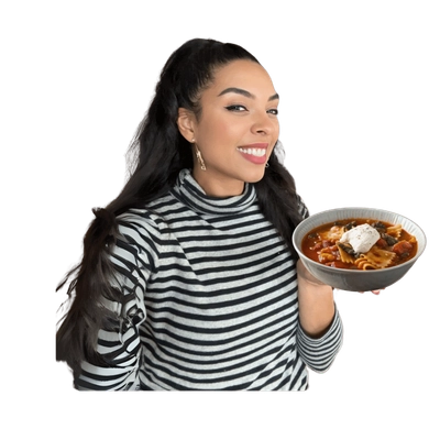 Woman smiling with bowl of hearty lasagna soup, wearing black and white striped shirt.