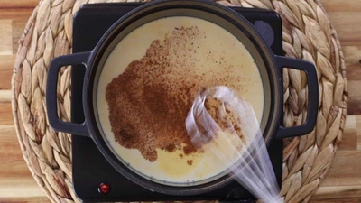 Creamy rice pudding with cinnamon being stirred in a pot on a stove.
