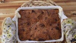 Freshly baked apple crumble in a white dish on a wooden table, with oven mitts holding it.