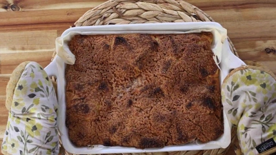 Freshly baked apple crumble in a white dish on a wooden table, with oven mitts holding it.