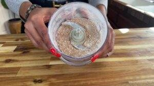 Hands holding a food processor with ground almonds on wooden table, perfect for baking or cooking recipes.
