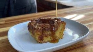 Close-up of a delicious bread pudding with syrup poured over, served on a white plate on a wooden table.