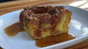 Slice of cinnamon sugar French toast casserole topped with syrup on a white plate, perfect breakfast treat.