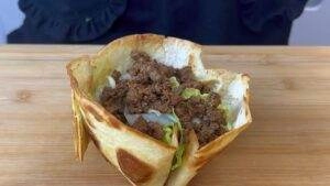 Crunchy taco bowl filled with seasoned beef and fresh lettuce on a wooden board, perfect for a tasty meal.