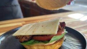 Close-up of a grilled chicken burger with cheese, tomato, and lettuce on a black plate, ready to be served.