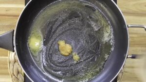 Melting butter and garlic paste sizzling in a black frying pan on a wooden kitchen table.
