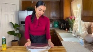 Woman in red shirt wrapping a dish with foil in a cozy kitchen setting.