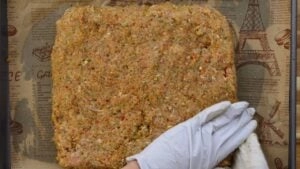 Gloved hand shaping seasoned minced chicken mixture on parchment paper.