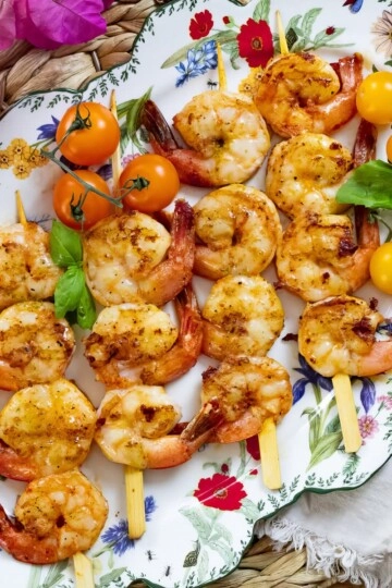 Grilled shrimp skewers with cherry tomatoes on a decorative plate, garnished with fresh basil leaves.