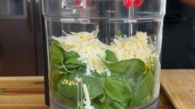 Food processor with fresh basil leaves and grated cheese, ready to make homemade pesto.