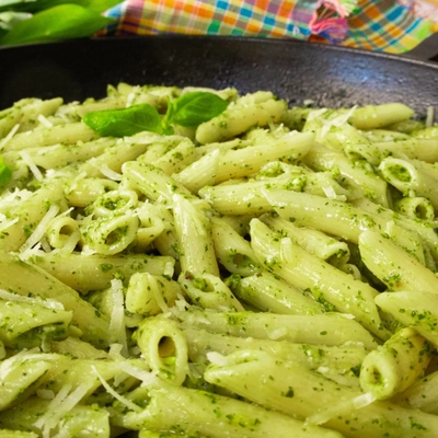 Creamy pistachio pesto penne pasta garnished with fresh basil leaves and parmesan cheese in a black skillet.