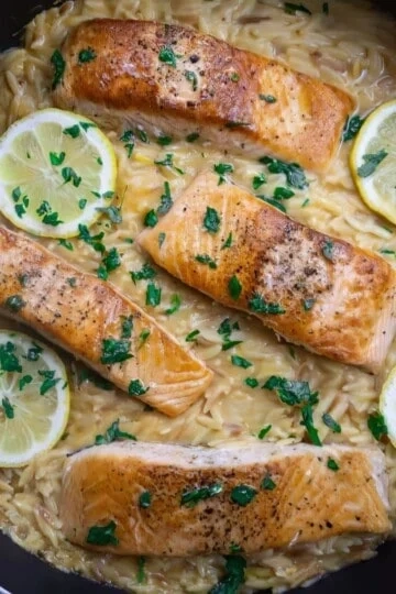 Pan-seared salmon with lemon slices on creamy orzo pasta, garnished with fresh parsley.