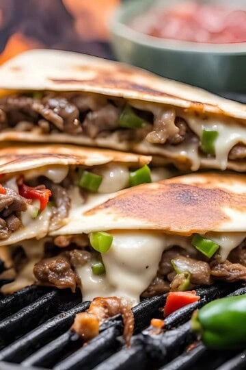 Grilled quesadillas with melted cheese, beef, and peppers on a barbecue grill with hot sauce in the background.