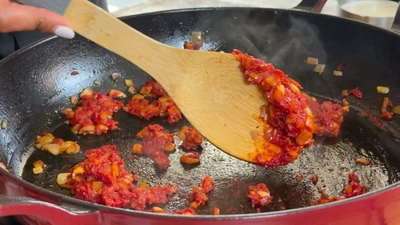 Cooking onions and tomatoes in a pan with a wooden spoon.
