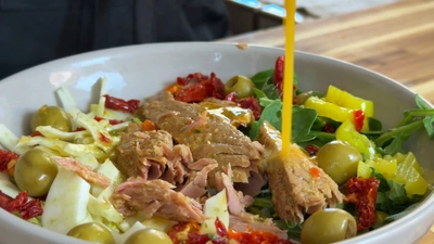 Fresh salad with tuna, olives, and peppers drizzled with oil.
