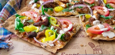 Fresh shawarma pizza topped with tomatoes, peppers, onions, and greens on printed parchment paper.