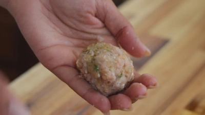 Hand holding seasoned meatball mixture.