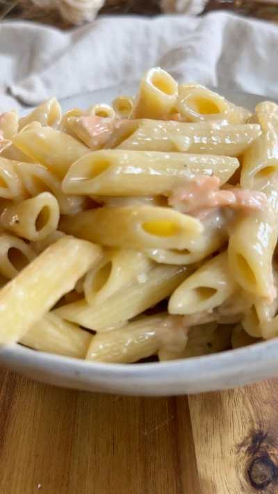 Creamy penne pasta with salmon in a white bowl on a wooden table.