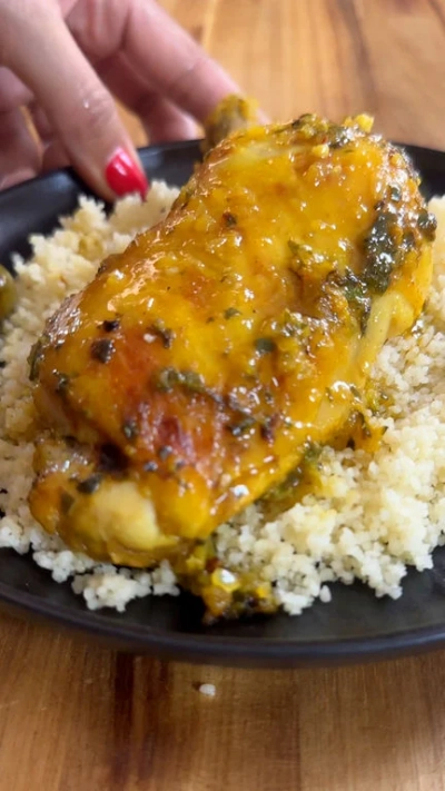 Chicken with sauce on couscous, served on a black plate, being gently placed by a hand.