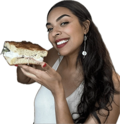 Smiling woman holding a large sandwich with layers of meat and lettuce.