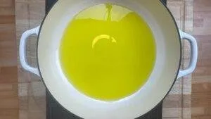 Overhead view of a white pot with hot olive oil on a wooden surface, ready for cooking.
